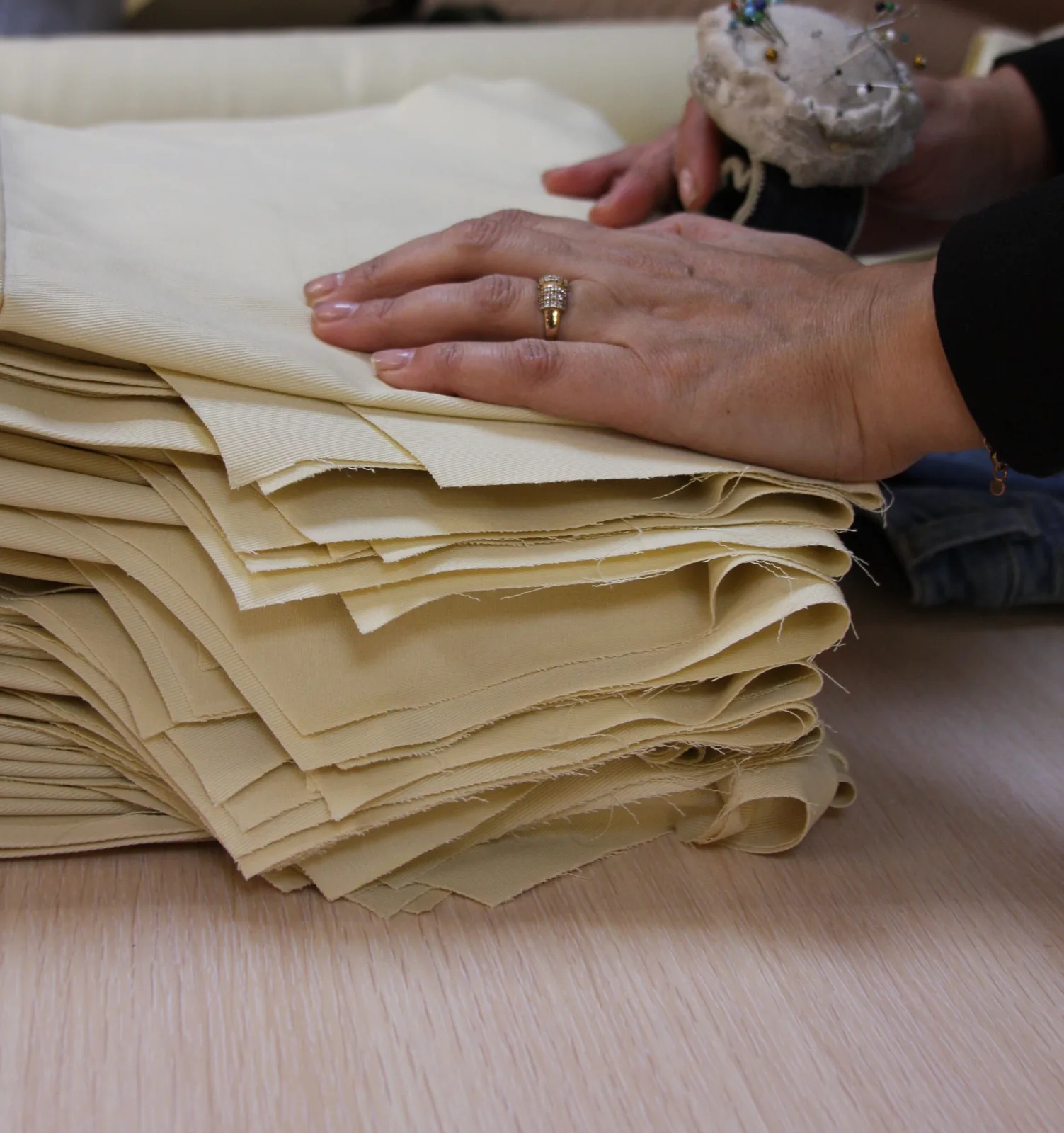 A stack of cut twill panels with raw, fraying edges, a hand squaring the pile