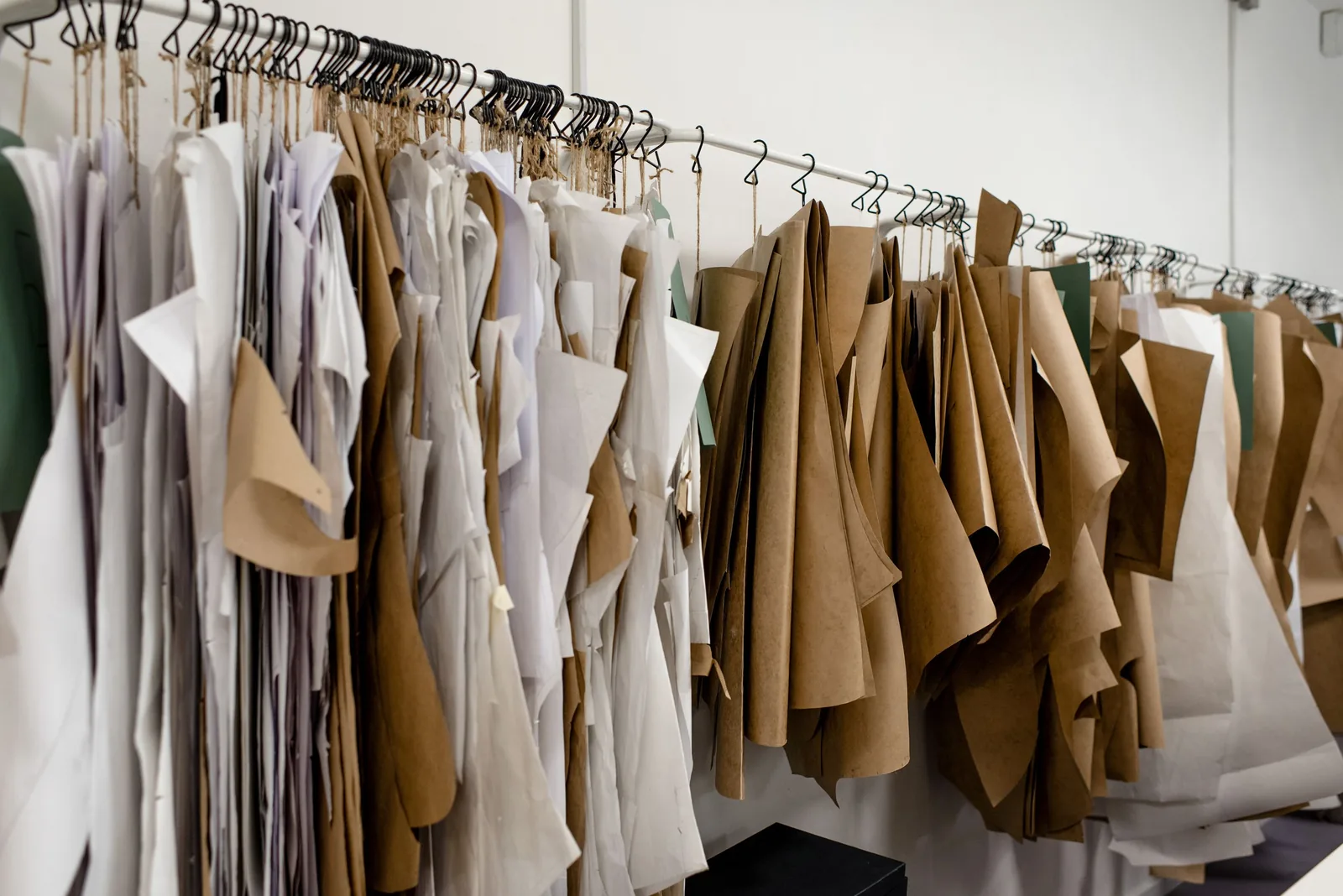 Kraft-paper and white paper pattern pieces hanging from hooks along a long rail against a white wall