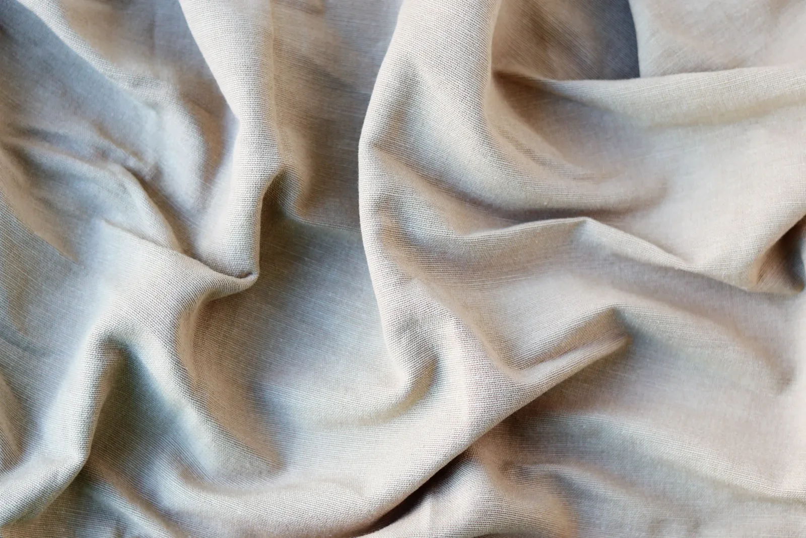 Close-up of crumpled light beige woven cotton cloth in soft folds, the fine weave visible on the surface
