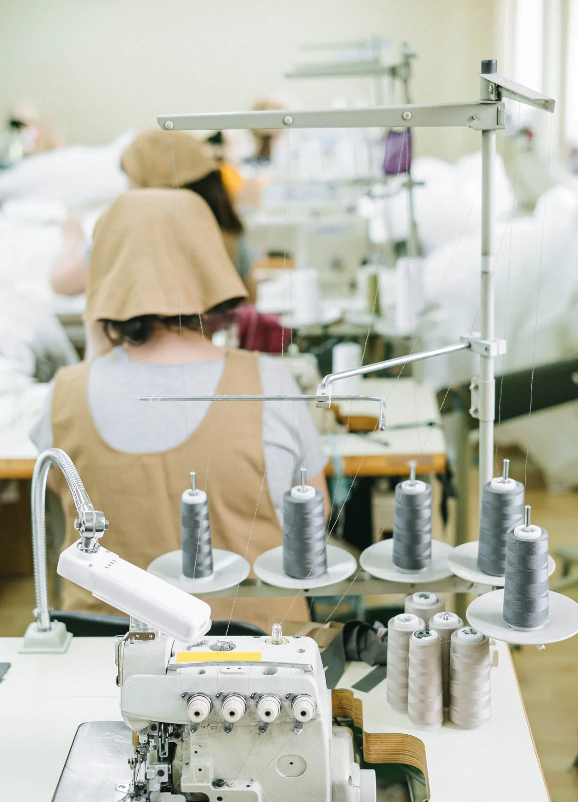 An overlock station with thread cones on a sewing floor, operators working at their machines behind it