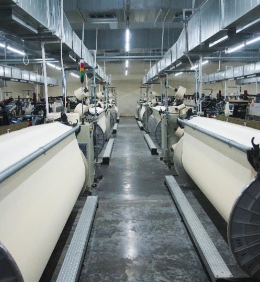 An aisle of power looms in Donear's weaving shed, greige fabric on the beams