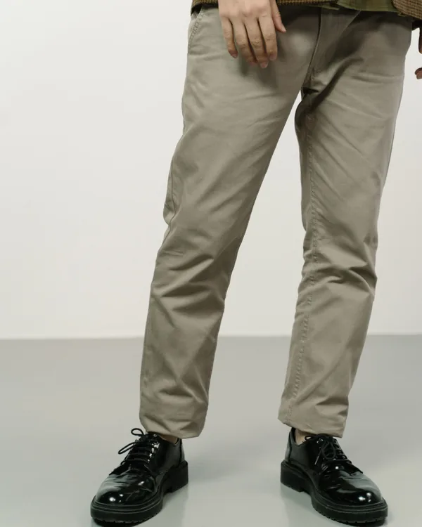 Taupe cotton twill chinos with a slim straight leg, worn with black lace-up shoes and shown from the waist down against a plain light wall