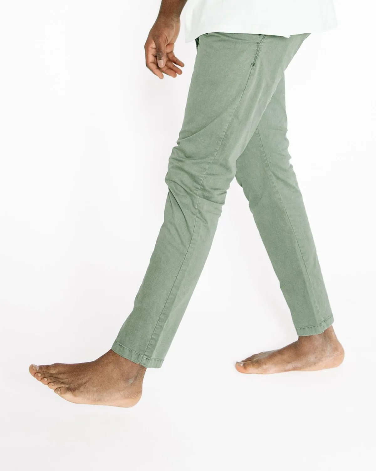 Sage green cotton twill chinos with a slim tapered leg and stitched hems, shown side-on in a walking stride against a plain white background