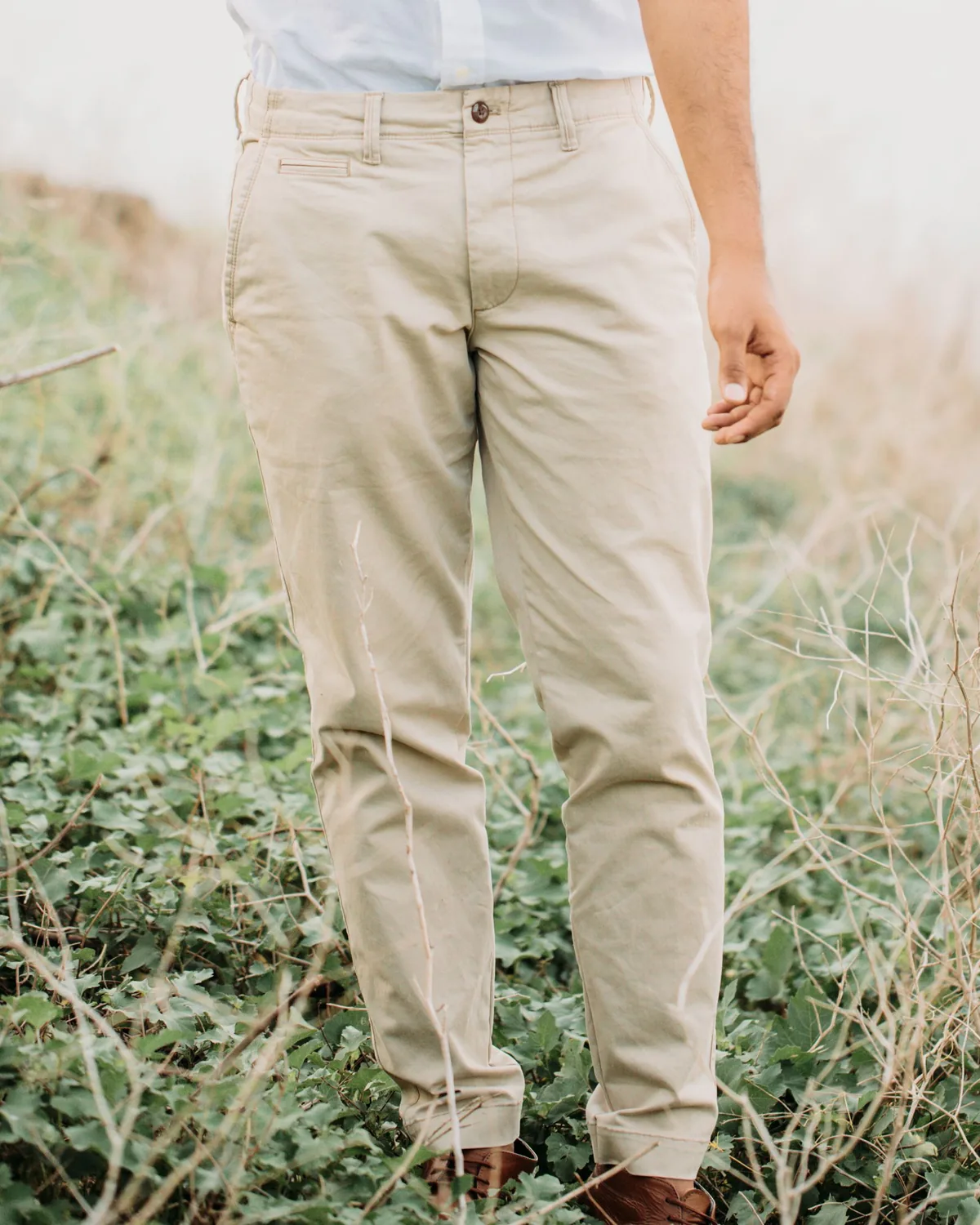 Beige cotton chinos with a buttoned waistband, belt loops, slanted side pockets and a welt coin pocket, worn with a tucked light shirt and shown from the waist down