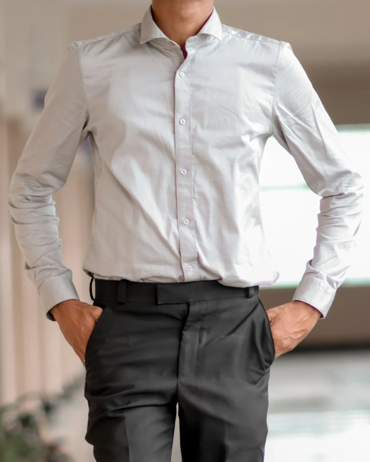 Light grey long-sleeve dress shirt with a cutaway collar, tucked into charcoal trousers, shown on a model from the neck down in a bright corridor