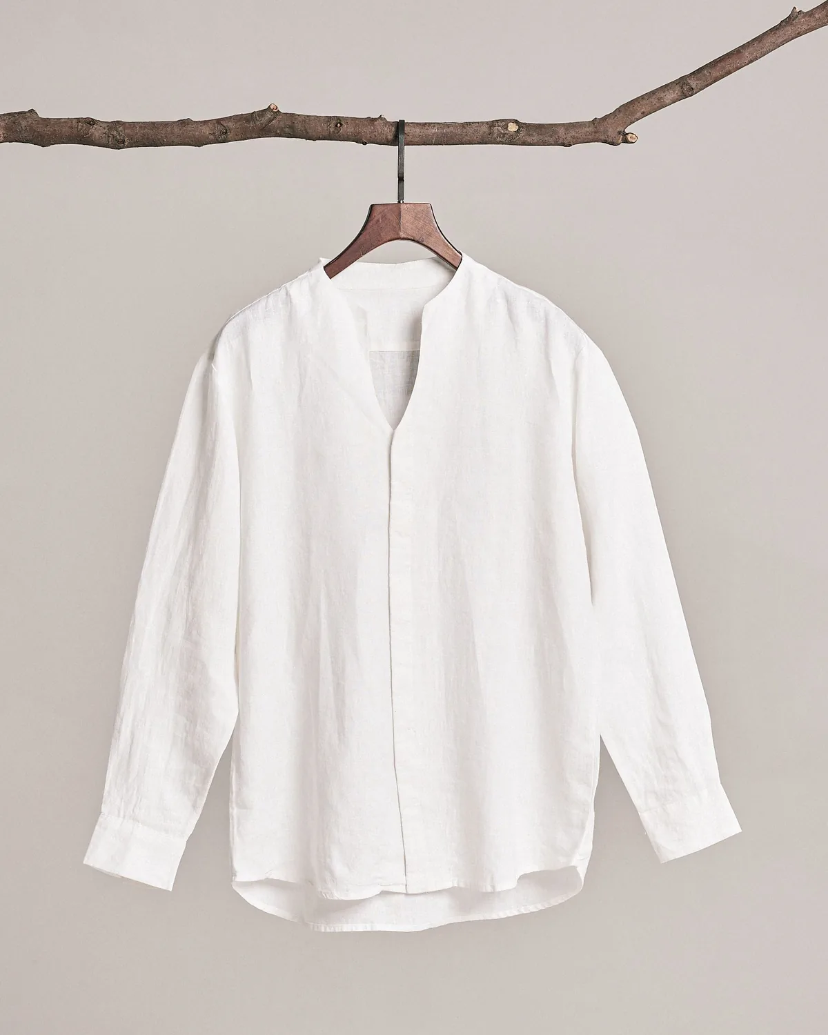 White long-sleeve linen shirt with notched band collar and concealed placket on a wooden hanger