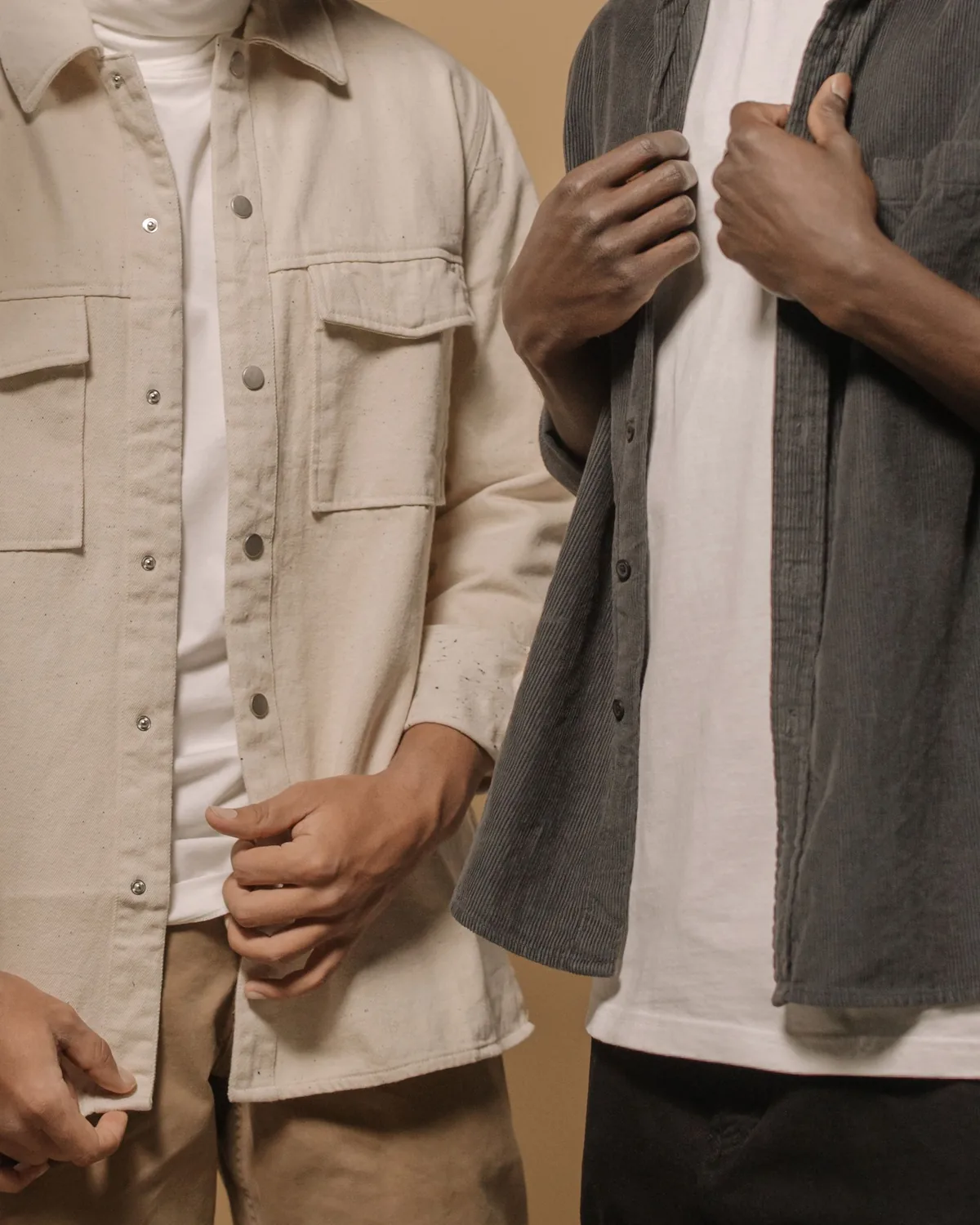 Ecru canvas overshirt with a point collar, press-stud front and two flap chest pockets, worn open over a white T-shirt beside a charcoal corduroy overshirt, both cropped at the neck on a warm beige background
