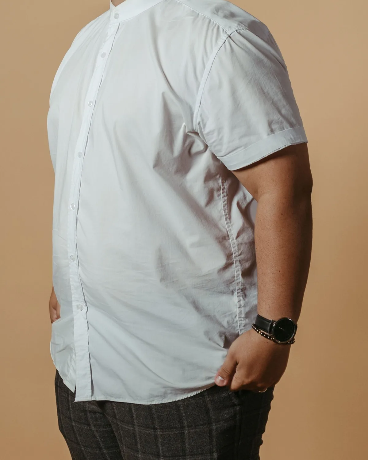 White short-sleeve shirt with a band collar and turned-up sleeve hems, worn untucked, cropped below the chin on a warm tan studio background