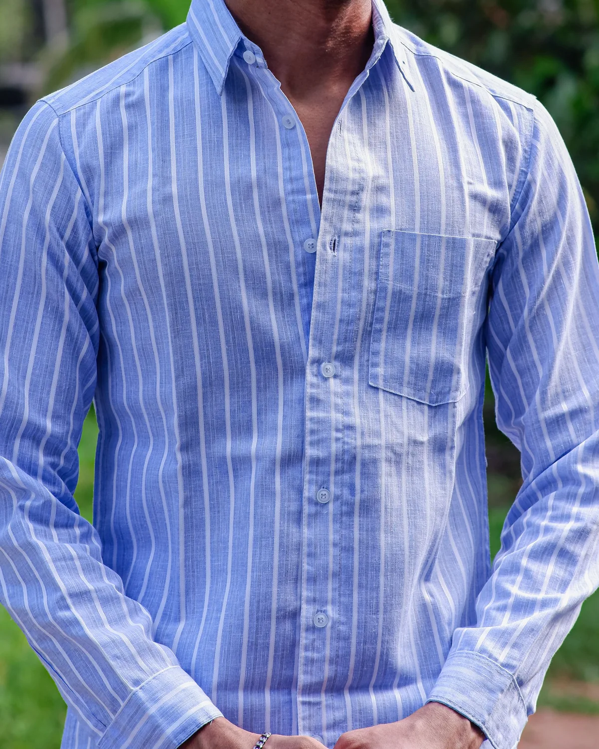 Light blue long-sleeve shirt with white candy stripes and a chest pocket, shown from the neck down against soft green foliage